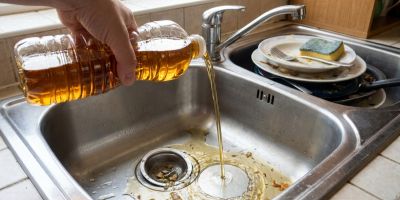 Person kippt Fett in den Abfluss, im Hintergrund steht Wasser in der Dusche